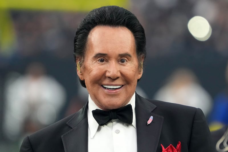 Wayne Newton, wearing a tuxedo, smiles on an NFL field